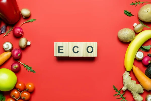 Top view of cubes with eco lettering near ripe fruits and vegetables on red background — Photo de stock