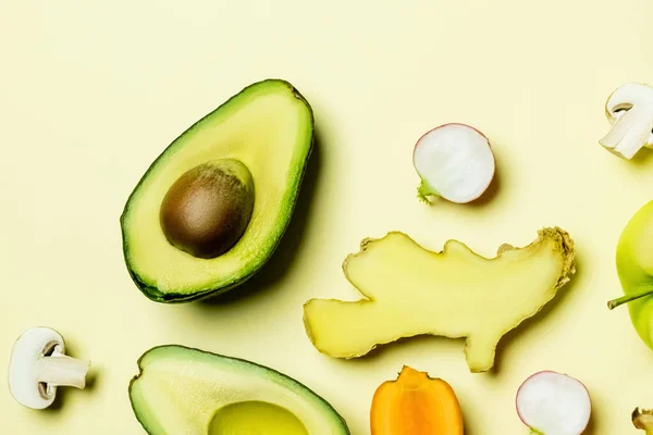 Top view of cut avocado near vegetables on yellow background — Stock Photo