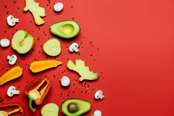 Flat lay of cut fruits and vegetables near peppercorns on red background - foto de stock