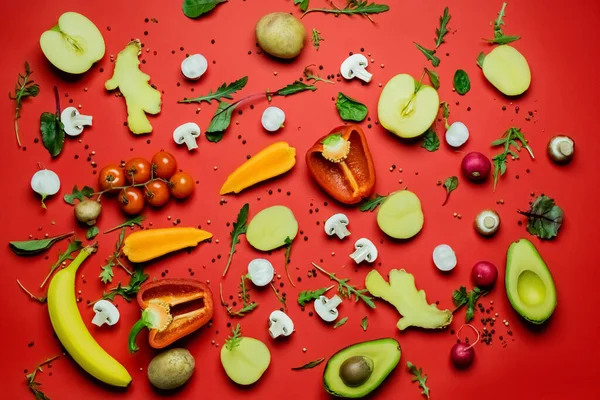 Top view of cut organic fruits, vegetables and spices on red background - foto de stock
