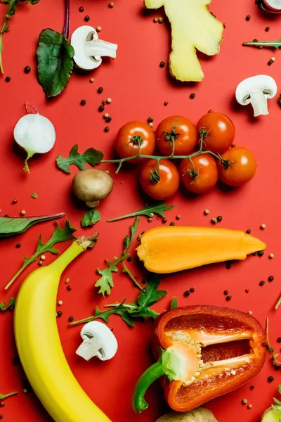 Vista superior de frutas y verduras maduras cerca de granos de pimienta sobre fondo rojo - foto de stock