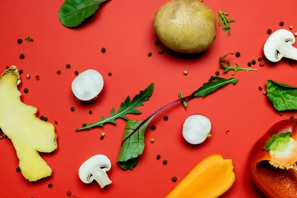 Top view of greens and peppercorns near cut organic food on red background — Stock Photo