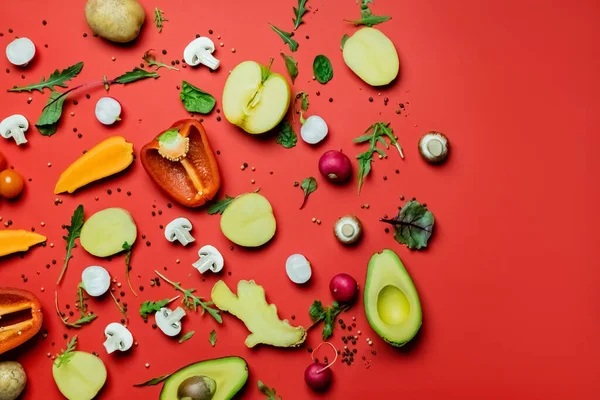 Vista superior de frutas y verduras cortadas cerca de granos de pimienta y verduras sobre fondo rojo - foto de stock