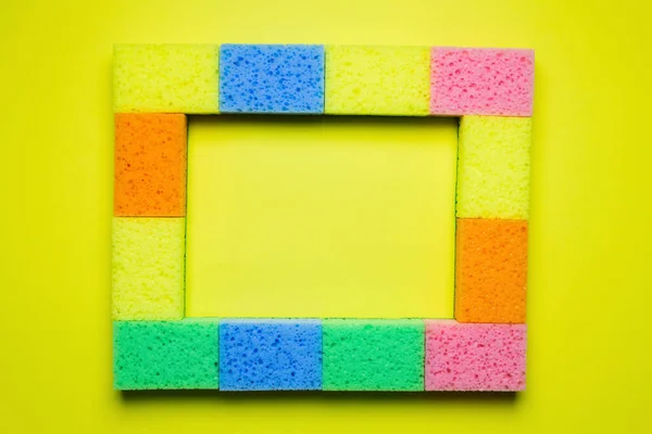 Rectangular frame of multicolored sponges on yellow background, top view - foto de stock