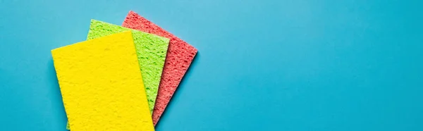 Top view of yellow, green and pink sponge cloths on blue background, banner — Photo de stock