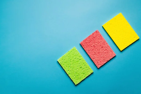 Top view of green, pink and yellow absorbent rags on blue background — стоковое фото