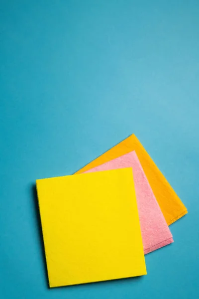 Top view of bright yellow, pink and orange dishrags on blue background — Photo de stock