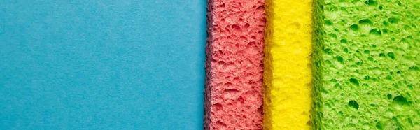 Close up view of green, yellow and pink sponge rags on blue background, banner — Photo de stock