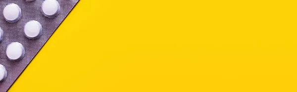 Vue rapprochée de la plaquette thermoformée avec des pilules blanches isolées sur jaune, bannière — Photo de stock