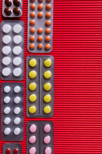 Top view of blister packs with different pills on crimson textured background — стоковое фото