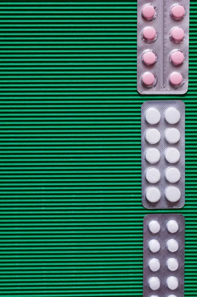 Vista superior de blisters con píldoras blancas y rosadas sobre fondo texturizado verde - foto de stock