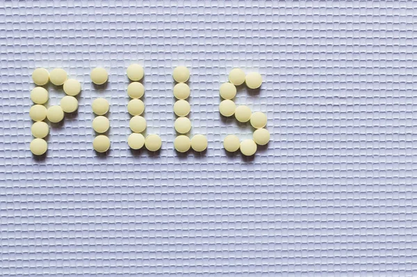 Top view of pills word made of yellow round shape medication on white textured background — Foto stock