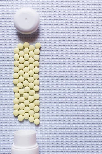 Pose plate de médicaments de forme ronde jaune près des bouteilles sur fond texturé blanc — Photo de stock