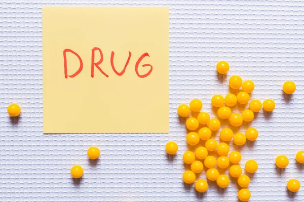 Top view of yellow round shape pills near paper note with drug lettering on white textured background — Stock Photo