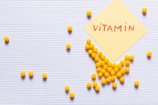 Top view of yellow round shape medication near paper note with vitamin lettering on white textured background — стоковое фото