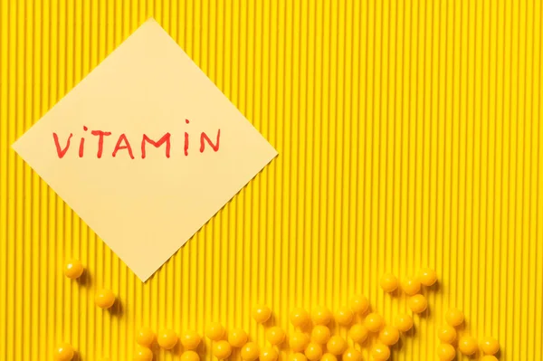 Top view of round shape medication near paper note with vitamin lettering on yellow textured background — стоковое фото