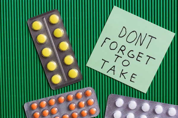 Top view of blister packs with pills near paper note with dont forget to take lettering on textured green background — стоковое фото