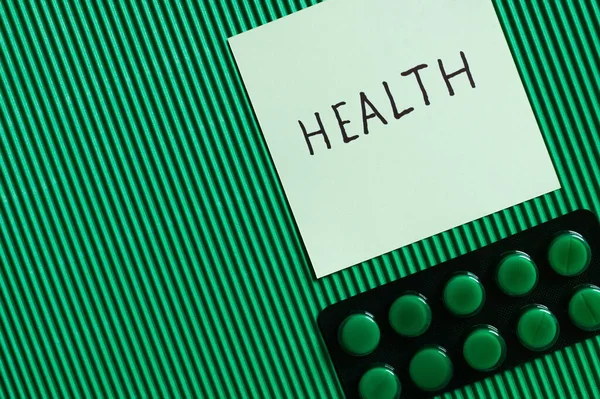 Vista dall'alto del blister con pillole vicino alla nota di carta con scritte sulla salute su sfondo verde testurizzato — Foto stock
