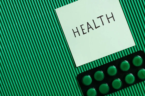 Top view of blister pack with pills near paper note with health lettering on textured green background — стоковое фото
