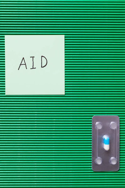 Top view of blister pack with pill near paper note with aid lettering on textured green background — Stock Photo