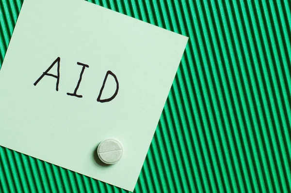 Top view of round shape pill near paper note with aid lettering on textured green background — Stock Photo