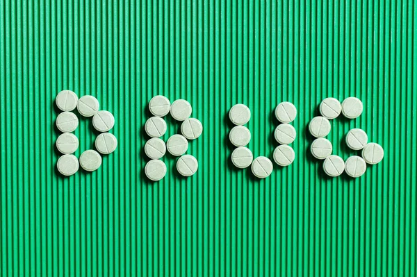 Top view of drug word made of yellow round shape medication on green textured background — Fotografia de Stock