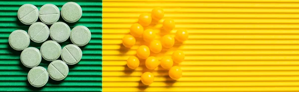 Top view of round shape pills and vitamins on textured green and yellow background, banner - foto de stock