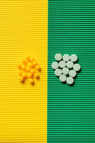 Top view of round shape pills and vitamins on textured green and yellow background — стоковое фото