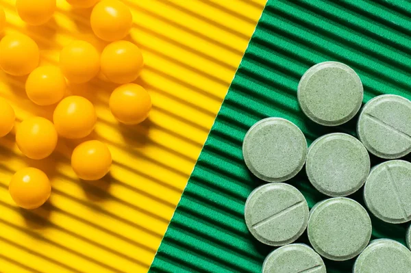 Close up view of round shape pills and vitamins on textured green and yellow background - foto de stock