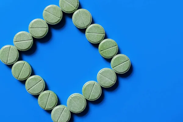 Top view of green pills in shape of rhombus on bright blue background - foto de stock