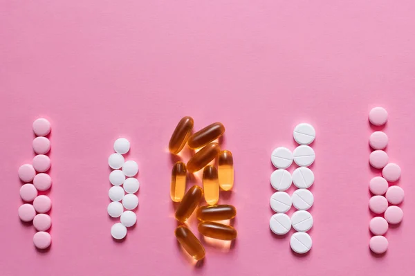 Flat lay view of different round shape pills and jelly capsules on pink background — Photo de stock