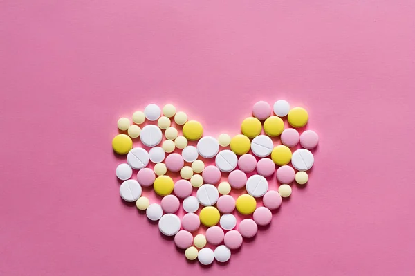 Flat lay view of different round pills in shape of heart on pink background — Fotografia de Stock