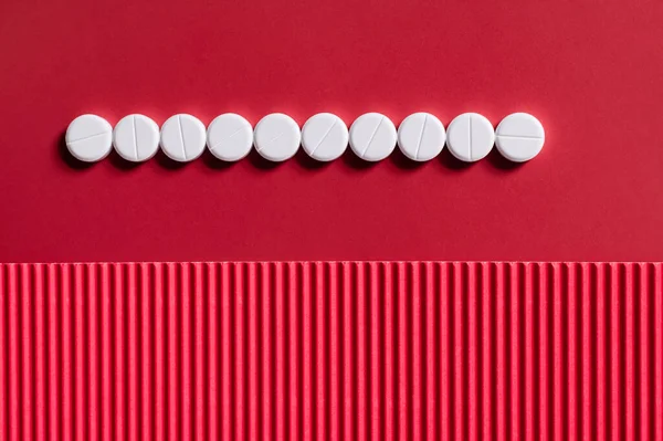 Vista superior de la fila con píldoras de forma redonda blanca sobre fondo carmesí y texturizado — Stock Photo