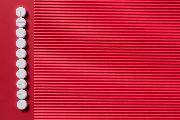Верхний вид вертикального ряда с белыми круглыми таблетками формы на малиновом и текстурированном фоне — стоковое фото