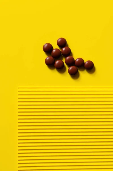 Вид зверху купа з таблетками темної круглої форми на жовтому і текстурованому фоні — стокове фото