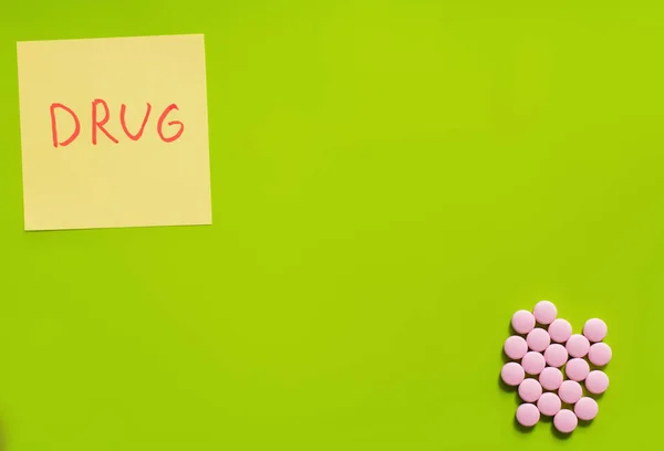 Top view of pink round shape medication near paper note with drug lettering on green background — Stock Photo