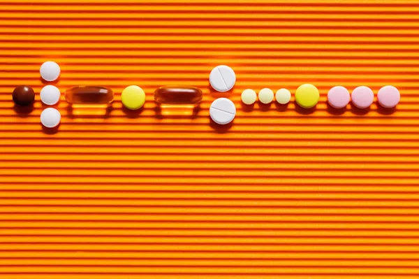 Disposición plana de diferentes píldoras sobre fondo texturizado naranja - foto de stock