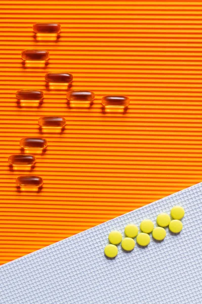 Flat lay of yellow pills on and jelly capsules on white and orange textured background — Stock Photo