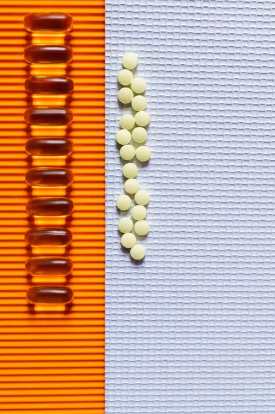 Disposición plana de filas con píldoras amarillas y cápsulas de gelatina sobre fondo texturizado blanco y naranja - foto de stock
