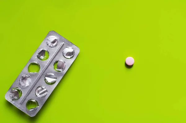 Вид сверху на использованный пузырь упаковки рядом с круглой формы таблетки на зеленом фоне — стоковое фото