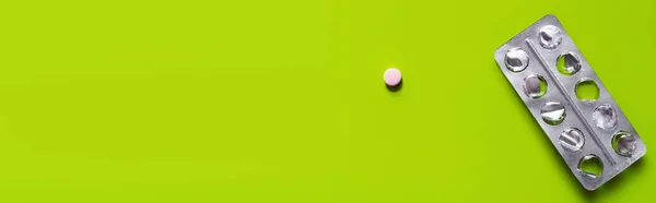Вид зверху використаної блістерної упаковки біля таблетки круглої форми на зеленому фоні, банер — стокове фото