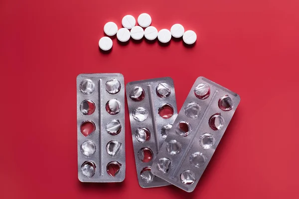 Top view of used blister packs near round shape pills on crimson background — стоковое фото