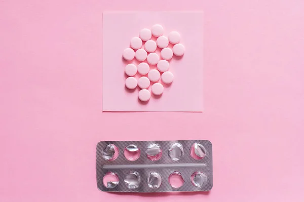 Top view of round shape pills on paper note near empty blister pack on pink — стоковое фото