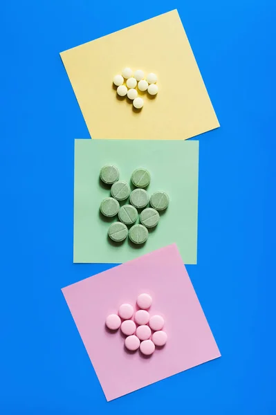 Vue du haut des pilules colorées de forme ronde sur des notes de papier isolées sur bleu — Photo de stock