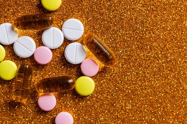 Vue du dessus de différentes pilules et capsules colorées sur fond doré brillant — Photo de stock