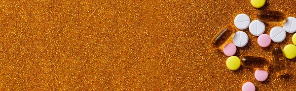 Vue du dessus de différentes pilules colorées sur fond doré brillant, bannière — Photo de stock