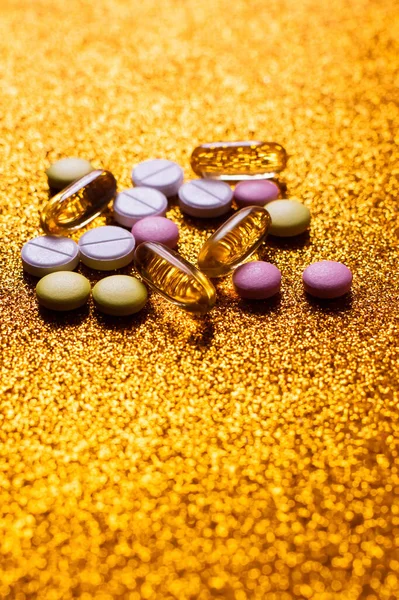 Different colorful pills and capsules on shiny golden background — Stockfoto