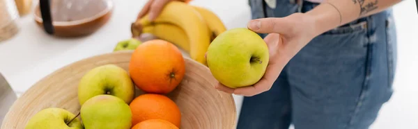 Vista recortada de la mujer sosteniendo manzana cerca del tazón con frutas frescas, pancarta - foto de stock