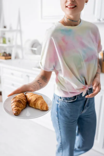 Cropped view of smiling woman holding plate with tasty croissants in kitchen — Photo de stock