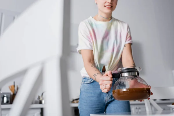 Partial view of smiling woman with coffee pot in kitchen on blurred foreground — Stock Photo